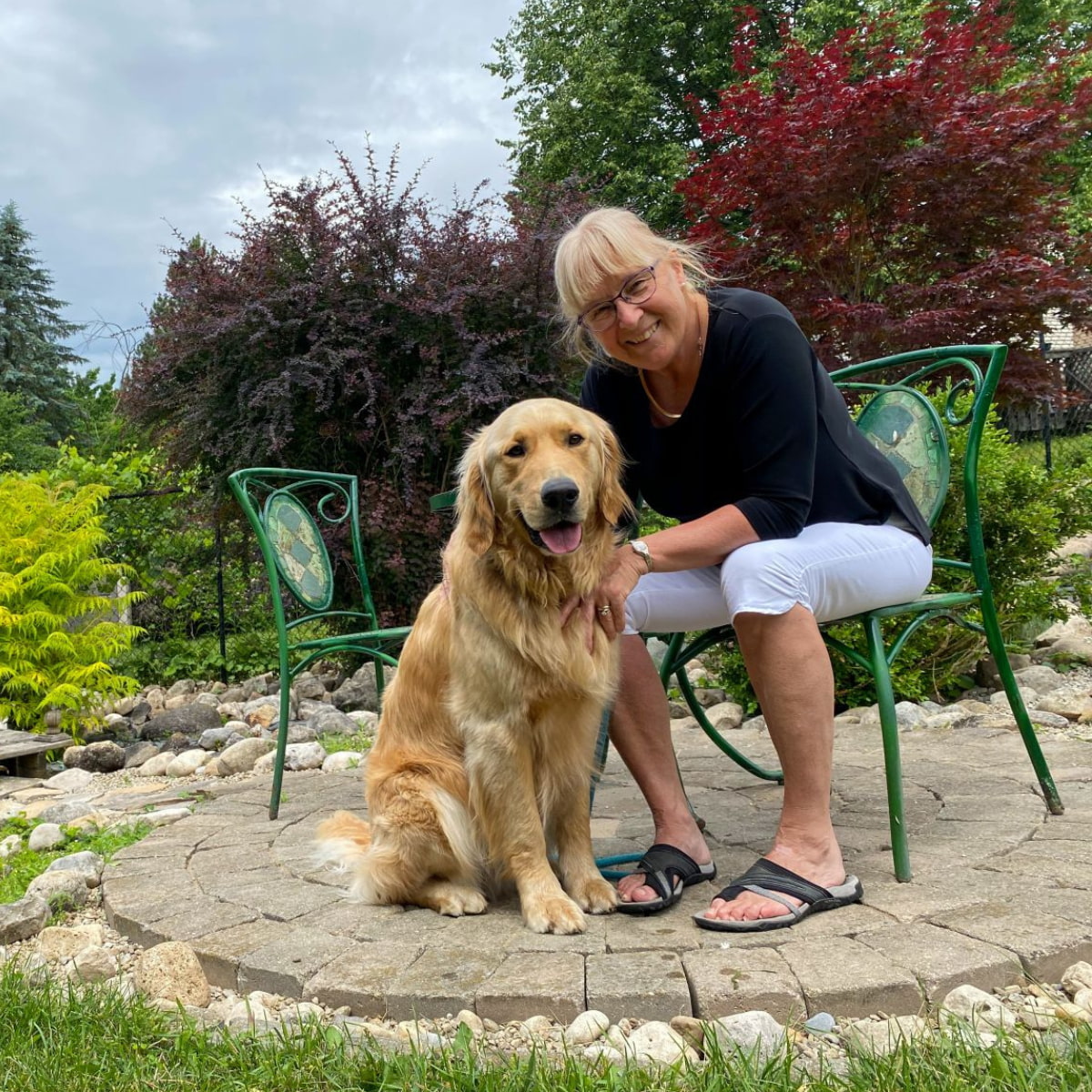 A woman with blonde hair sitting in a chair outside with a golden retriever sitting next to her