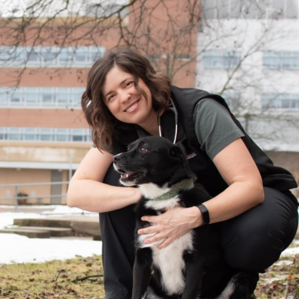 Woman staring at camera while kneeling and hugging black and white large dog in front of a building