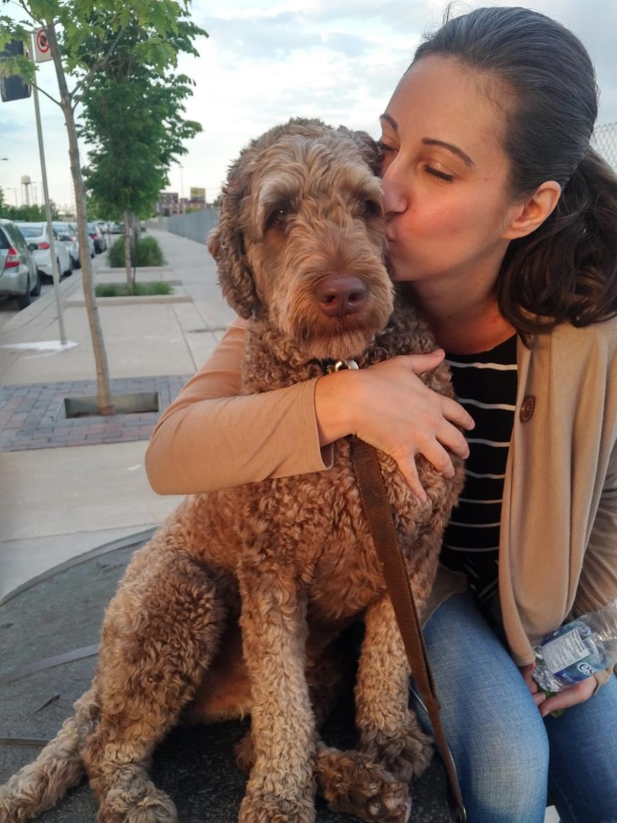 A woman with brown hair hugging and kissing a fluffy brown dog