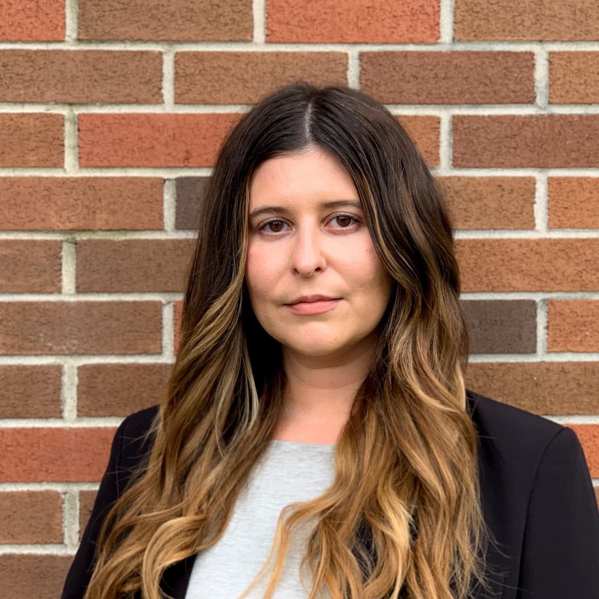 A woman with long hair looking at the camera and standing in front of a red-brick wall